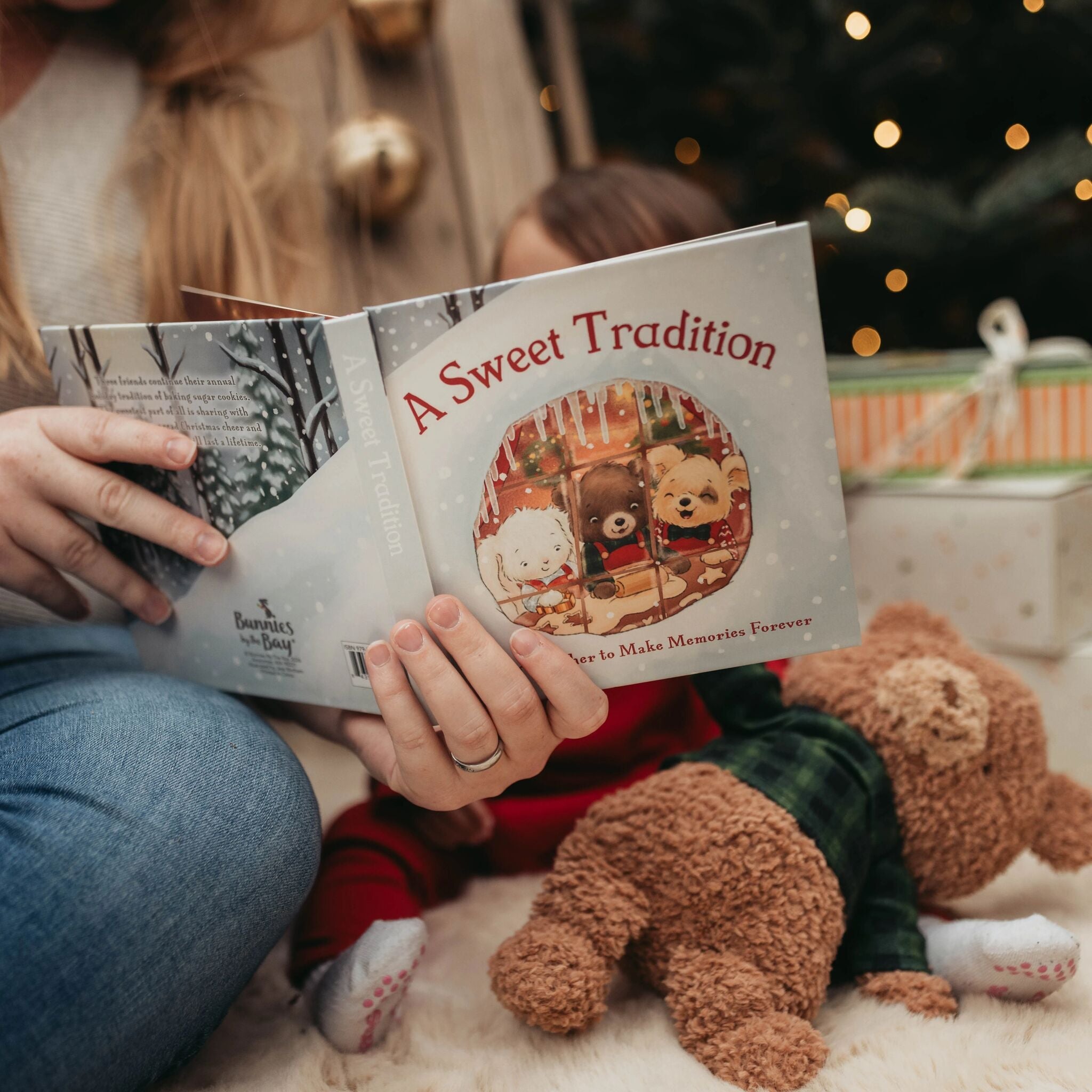 Person reading a book titled 'A Sweet Tradition' to a child with teddy bears around.