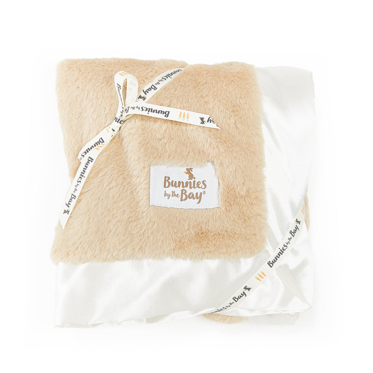 A folded plush beige blanket wrapped in a white ribbon printed with 'Bunnies by the Bay' and a matching brand patch on the front, set against a plain white background.