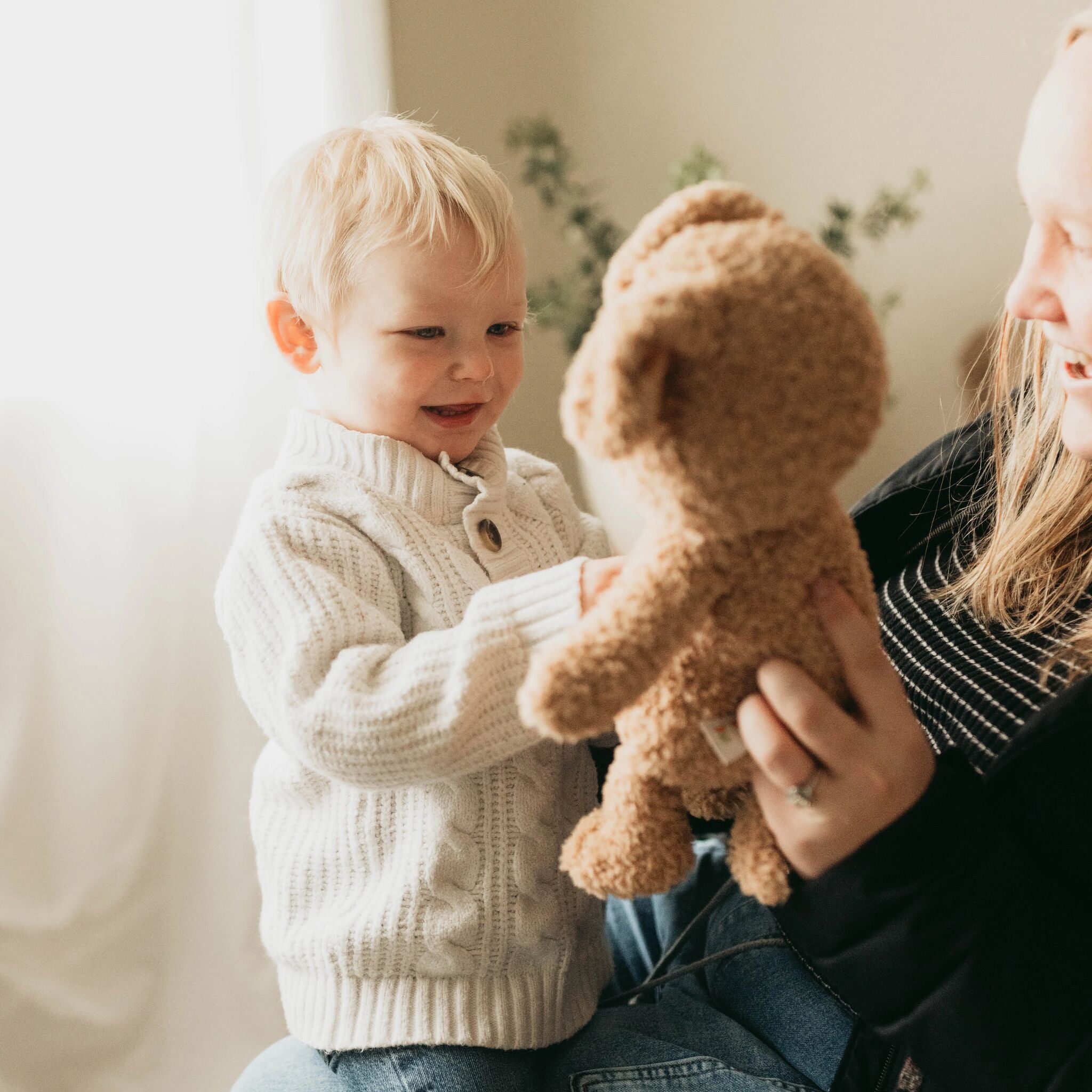 Child holding a teddy bear with an adult in a cozy indoor setting
